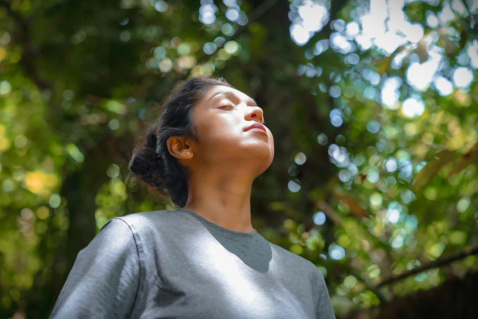 Mujer respirando profundamente con los ojos cerrados junto a un árbol